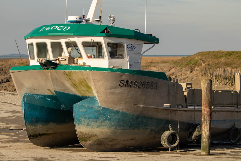 a green and white boat sitting on top of a sandy beach