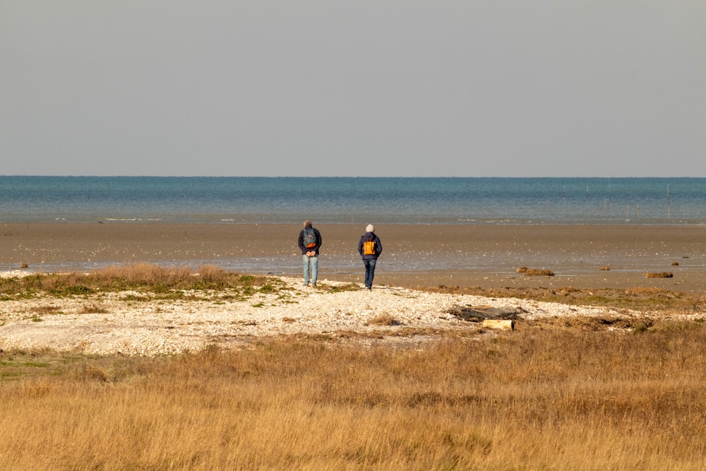 um par de pessoas em pé em cima de uma praia de areia