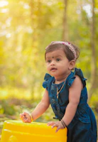 A toddler wearing a delicate heirloom dress made from a Bonnie Blue Designs® pattern, standing in a sunlit garden.