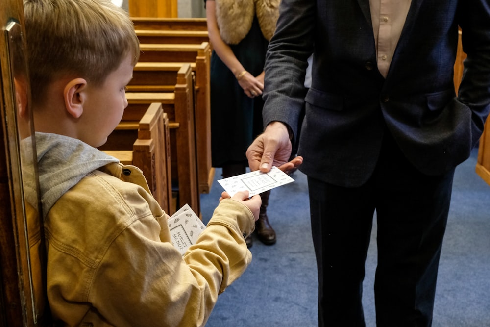 a boy in a suit handing something to a man in a suit