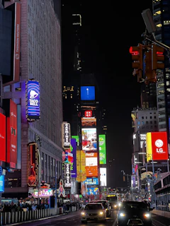 A row of illuminated digital boards lining a busy urban street during the evening rush hour.