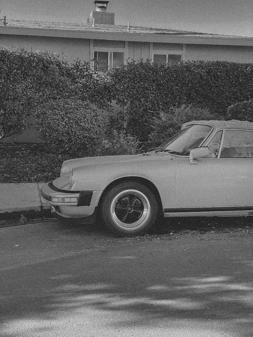 a black and white photo of a car parked in front of a house