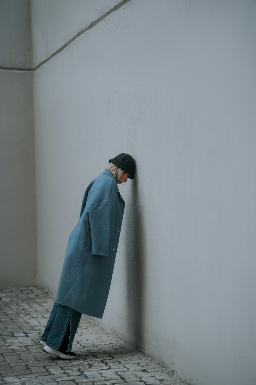 a person in a blue coat leaning against a wall