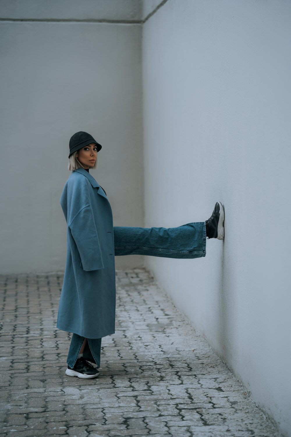 a woman in a blue coat leaning against a wall