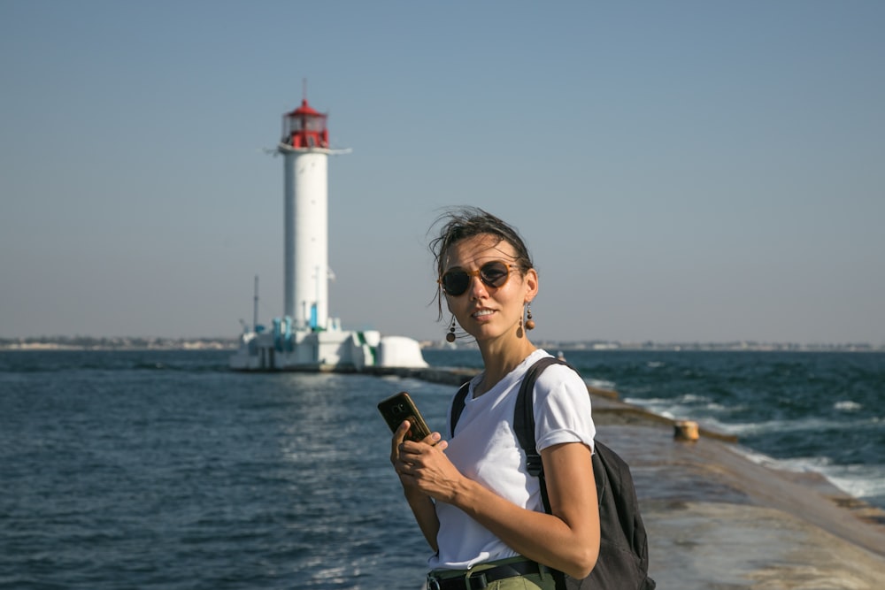 a woman holding a cell phone next to the ocean