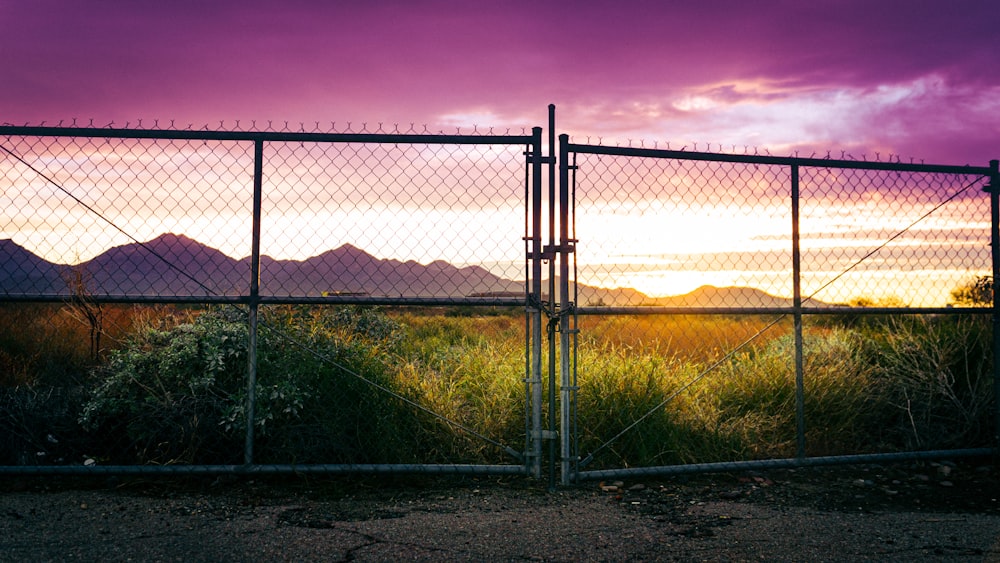 a fence with mountains in the background at sunset