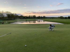 A golfer studying putting stats on a smartphone while standing on a green under a bright sunny sky.