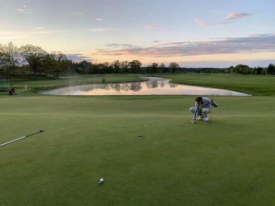 A golfer studying putting stats on a smartphone while standing on a green under a bright sunny sky.