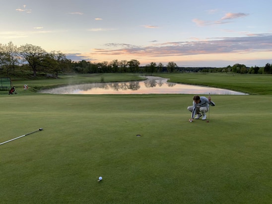 A golfer lining up a putt on a sunlit green with clubs and gear neatly arranged nearby.