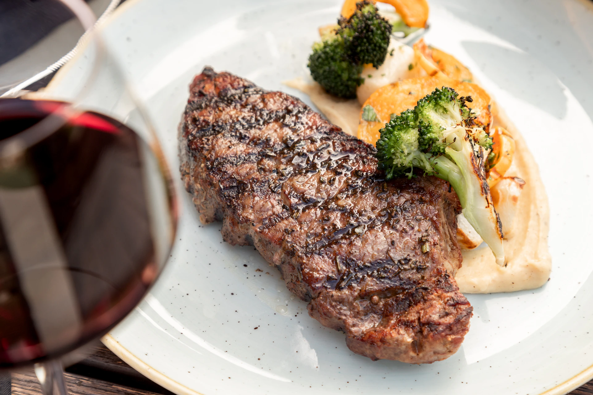 A warm, inviting image of a perfectly cooked steak resting beside roasted vegetables, with a glass of red wine softly blurred in the background.