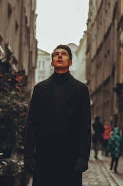 a man in a black coat standing on a street