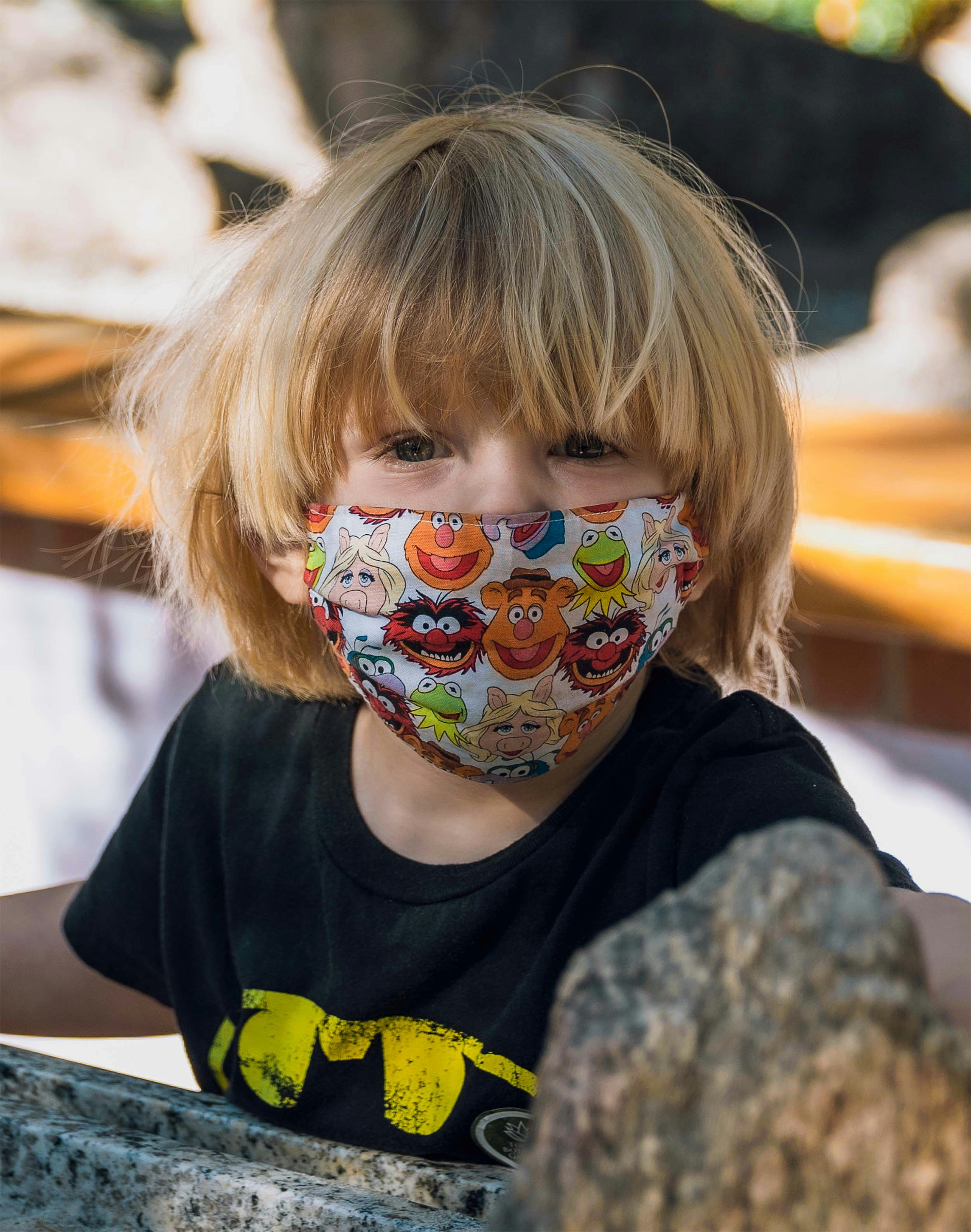 a little girl wearing a face mask with cartoon faces on it