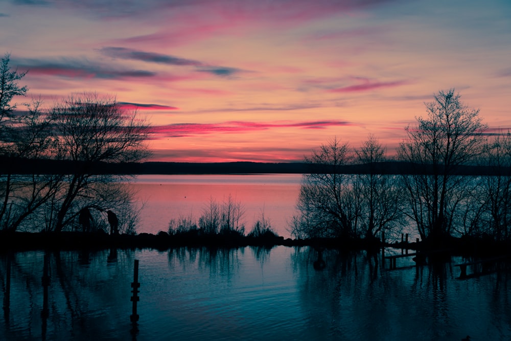 a sunset over a body of water with trees in the foreground