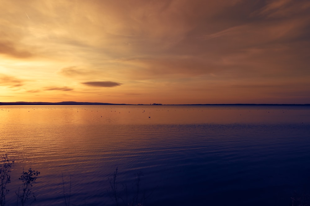 the sun is setting over a calm lake