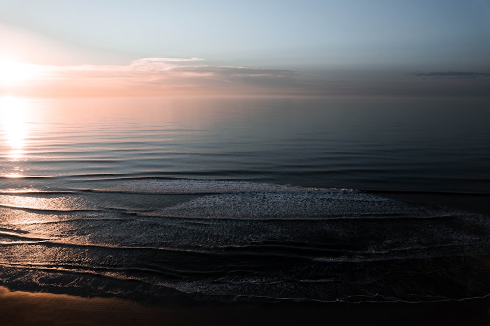 the sun is setting over the water on the beach