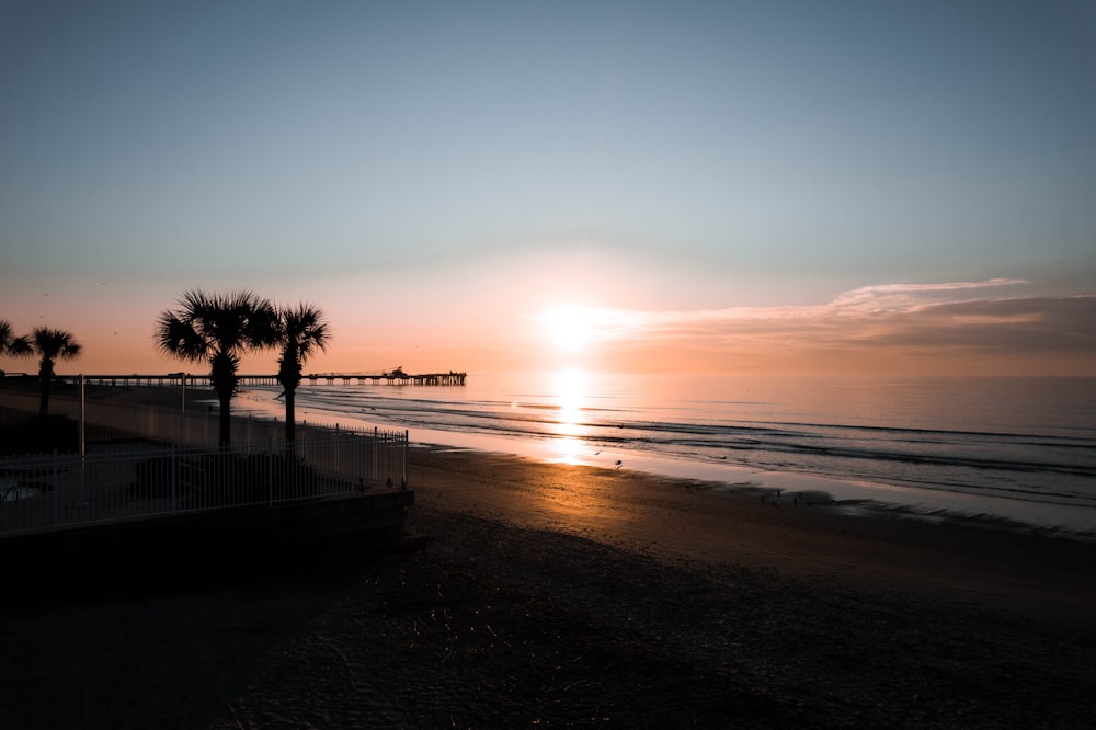 the sun is setting on the beach with palm trees