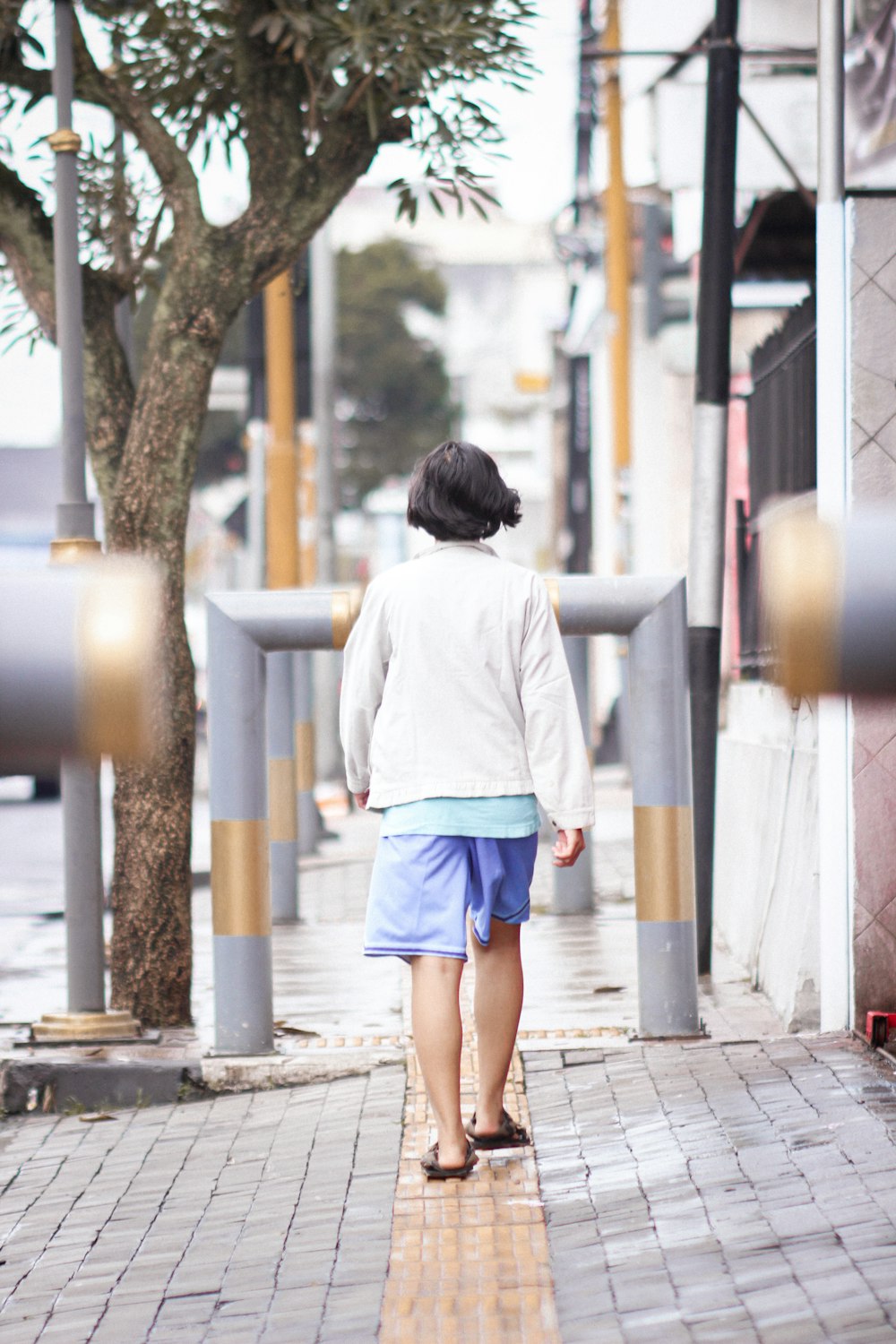 a woman walking down a sidewalk next to a tree