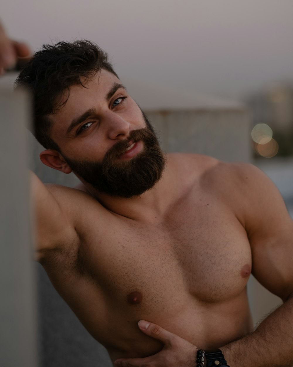 Un uomo a torso nudo con la barba appoggiata a un muro