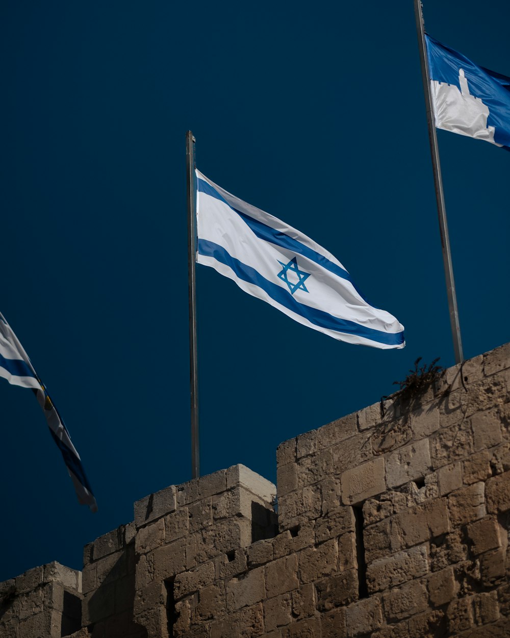 a brick wall with three flags flying in the wind