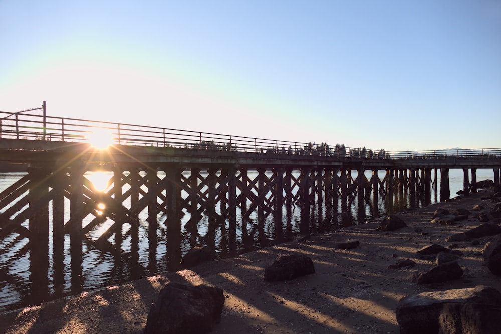 the sun is setting over a pier on the water