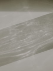 A textured surface with a shadow cast over it, creating a pattern. The shadow is elongated and shows variations in light intensity, giving a wavy appearance.