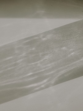 A textured surface with a shadow cast over it, creating a pattern. The shadow is elongated and shows variations in light intensity, giving a wavy appearance.