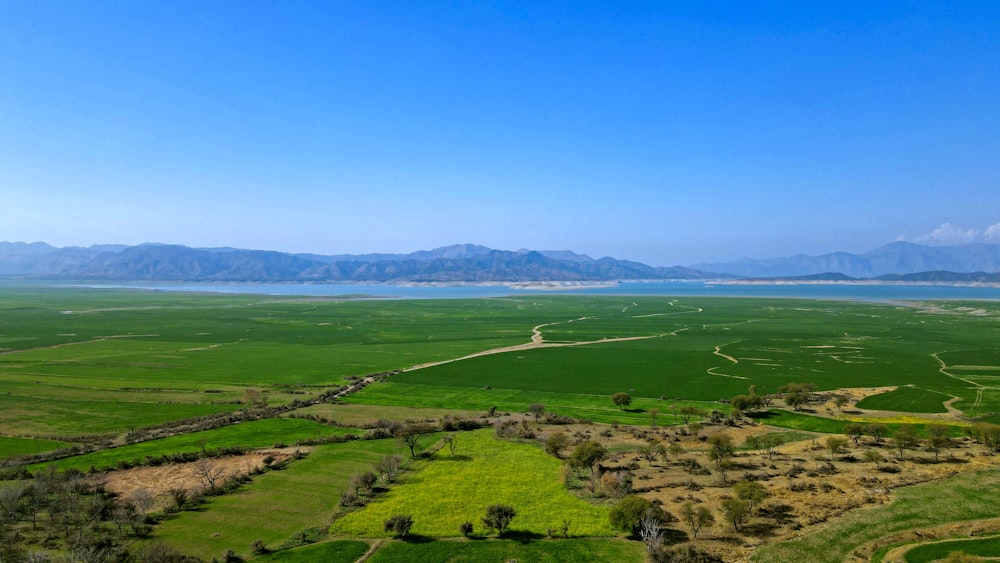 an aerial view of a green field with mountains in the background