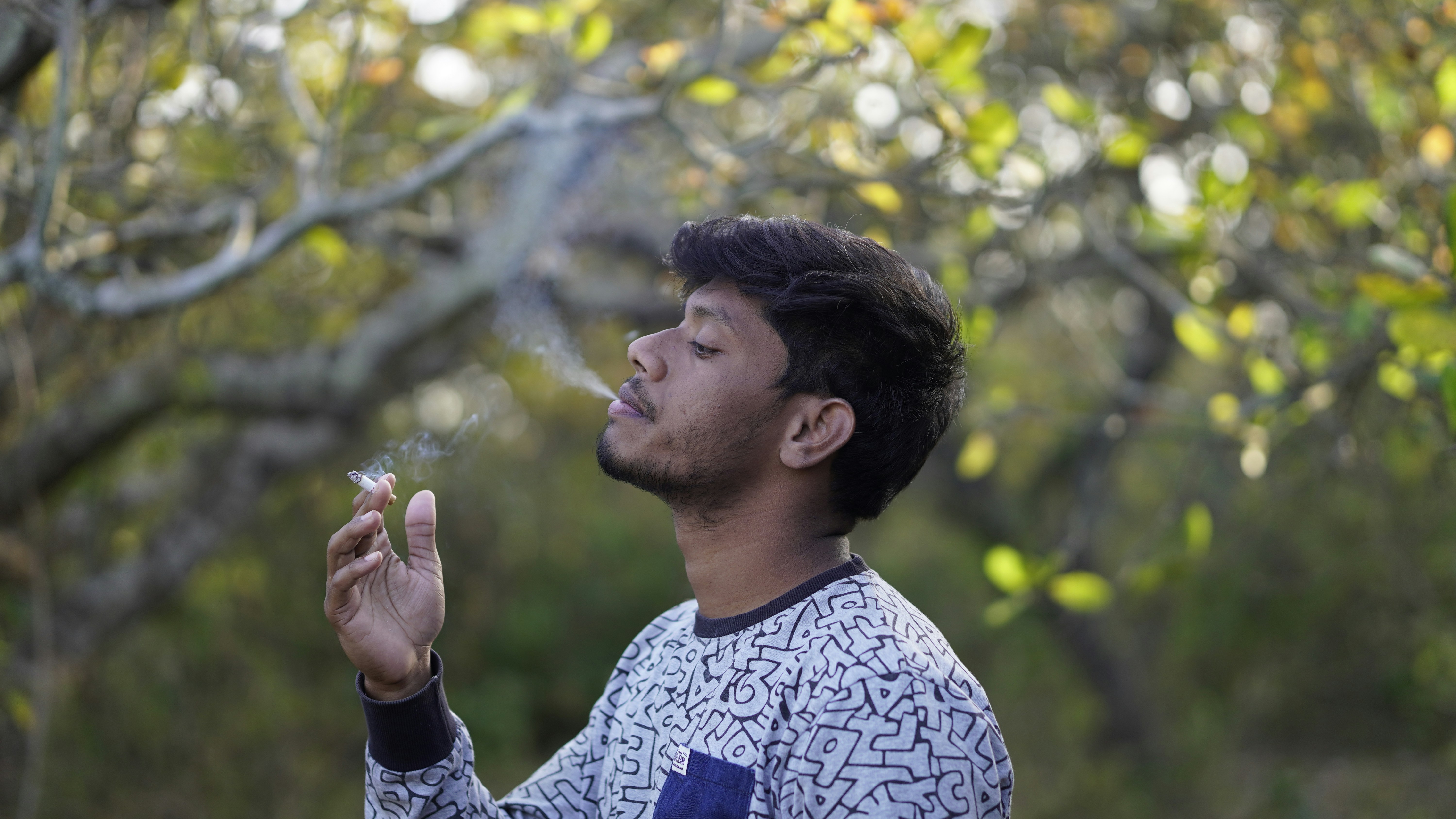 a man smoking a cigarette in front of a tree