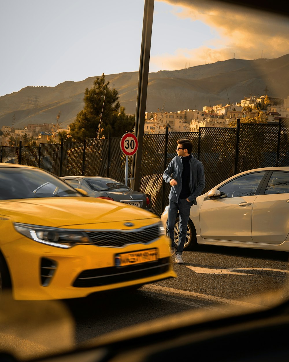 a man walking across a parking lot next to a yellow car