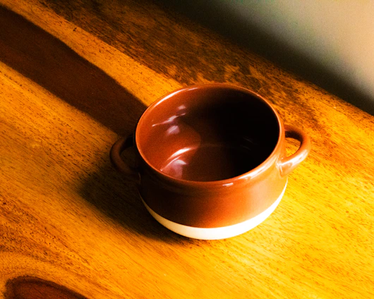 A vibrant, handmade ceramic mug resting on a wooden table bathed in warm sunlight.