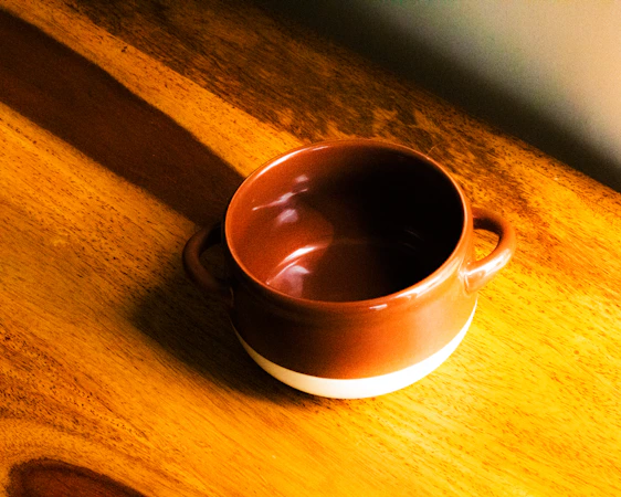 A bright, hand-thrown stoneware mug resting on a wooden table with soft natural light highlighting its colorful glaze.