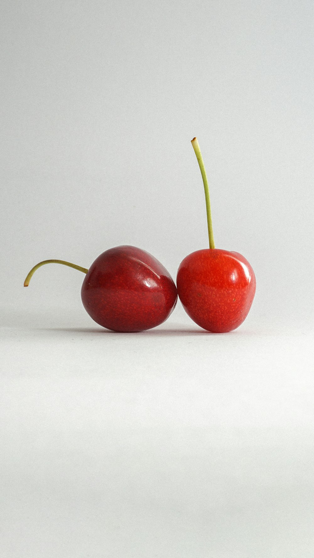 two cherries sitting side by side on a white surface