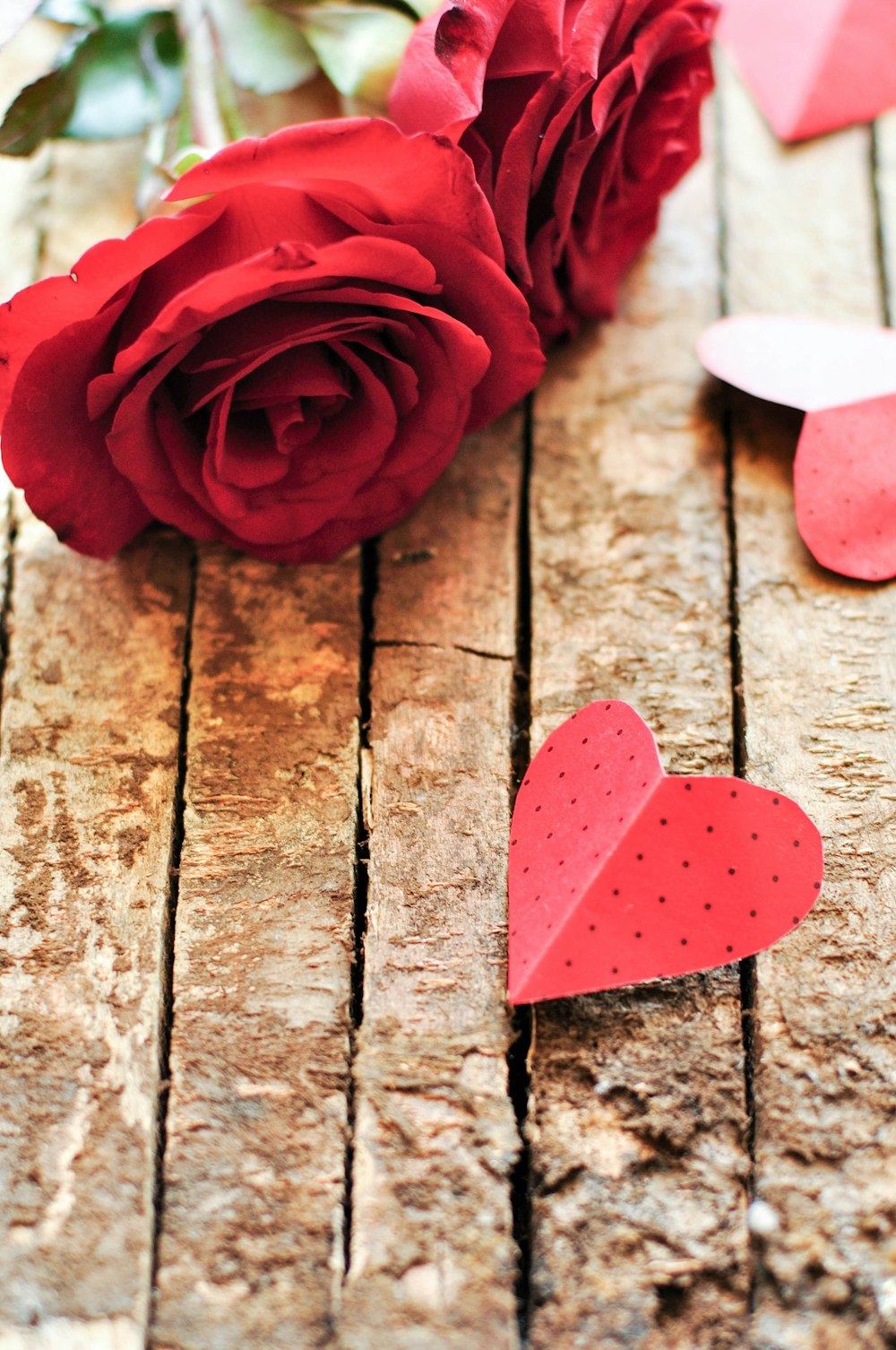 a red rose and a paper heart on a wooden table