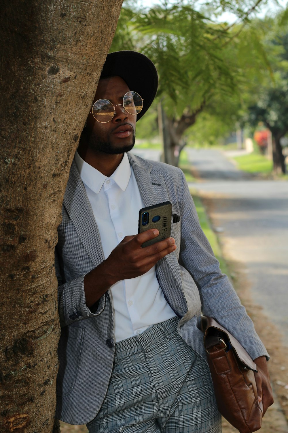 a man in a suit leaning against a tree looking at his cell phone