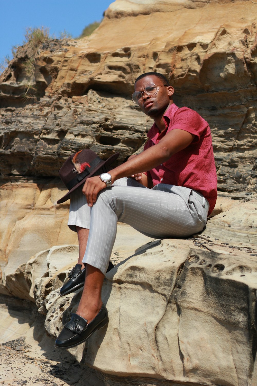 a man in a red shirt and hat sitting on a rock