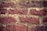 Rough, textured red bricks are stacked in a horizontal pattern, separated by light-colored mortar. The surface of the bricks appears weathered and aged.