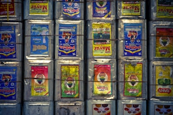 Rows of metal containers with colorful labels are stacked together, each secured by horizontal and vertical wires. The labels display vibrant designs and text in various languages.