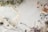 A collection of vintage sheet music is spread out on a textured, light-colored surface, accompanied by dried flowers and leaves. To the right, scissors and spools of thread add a crafting element to the scene.