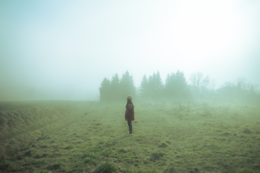 a woman standing in a foggy field with trees in the background