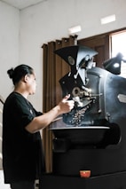A smiling coffee roaster inspecting beans in a rustic roasting facility.