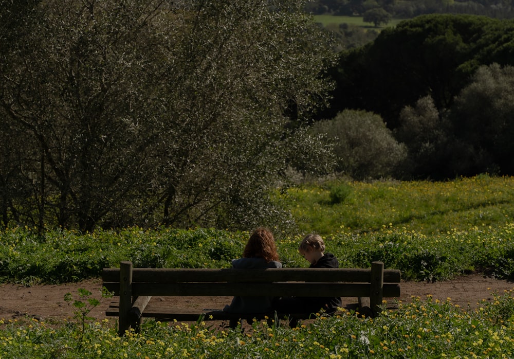 two people sitting on a bench in a field