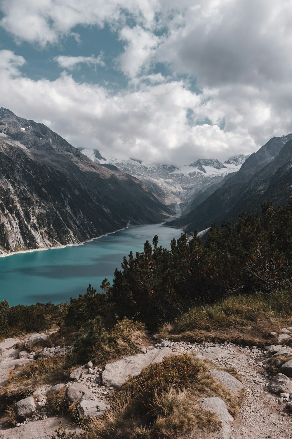 a lake surrounded by mountains under a cloudy sky