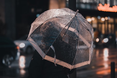 A person holding an open compact umbrella on a rainy city street.
