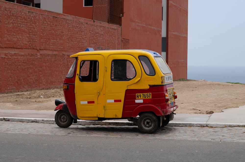 Un pequeño vehículo amarillo y rojo estacionado al costado de una carretera