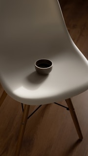 A minimalist white plastic chair with wooden legs on a clean white rug.