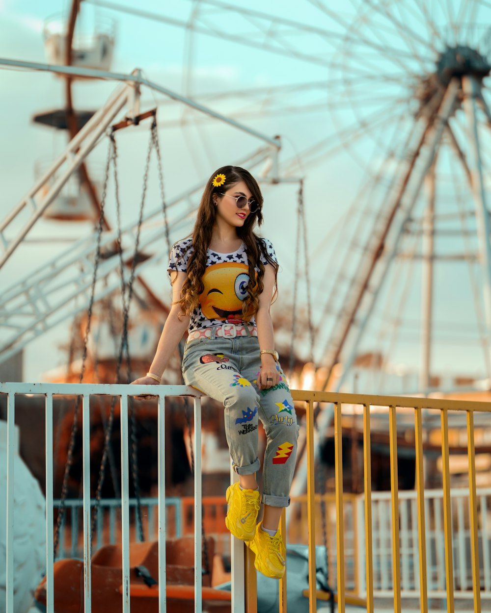 a woman sitting on a rail next to a ferris wheel