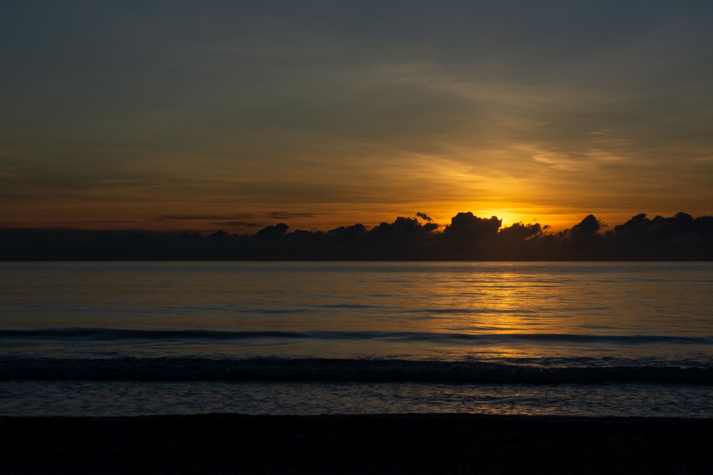 the sun is setting over the ocean with clouds