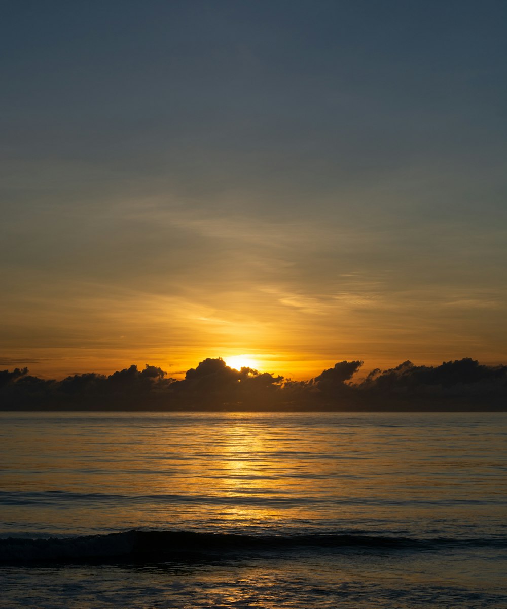 the sun setting over the ocean with clouds in the sky