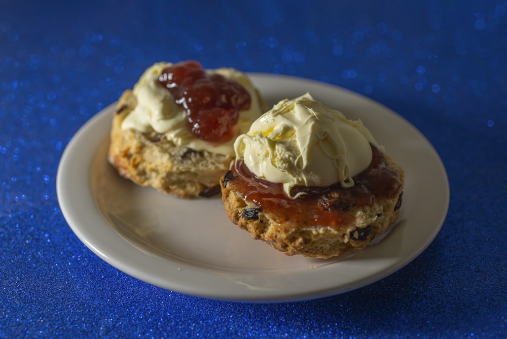 two scones with cream and jelly on a white plate