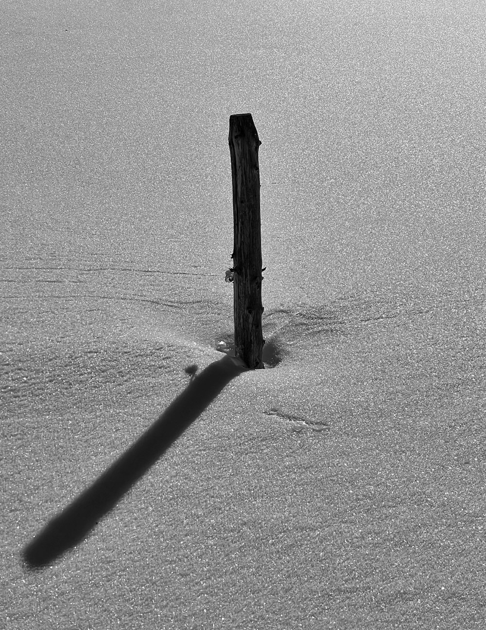 a black and white photo of a wooden post in the snow